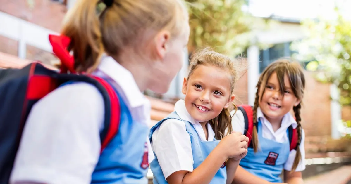 Happy schoolchildren in uniforms smiling and laughing together outdoors during a sunny day at school.
