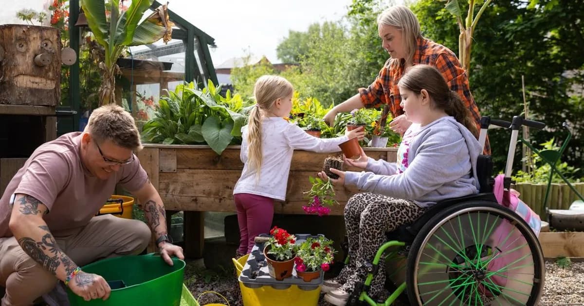 A diverse group of four people of varying ages and abilities gardening together in a community garden, tending to raised beds and potted plants.