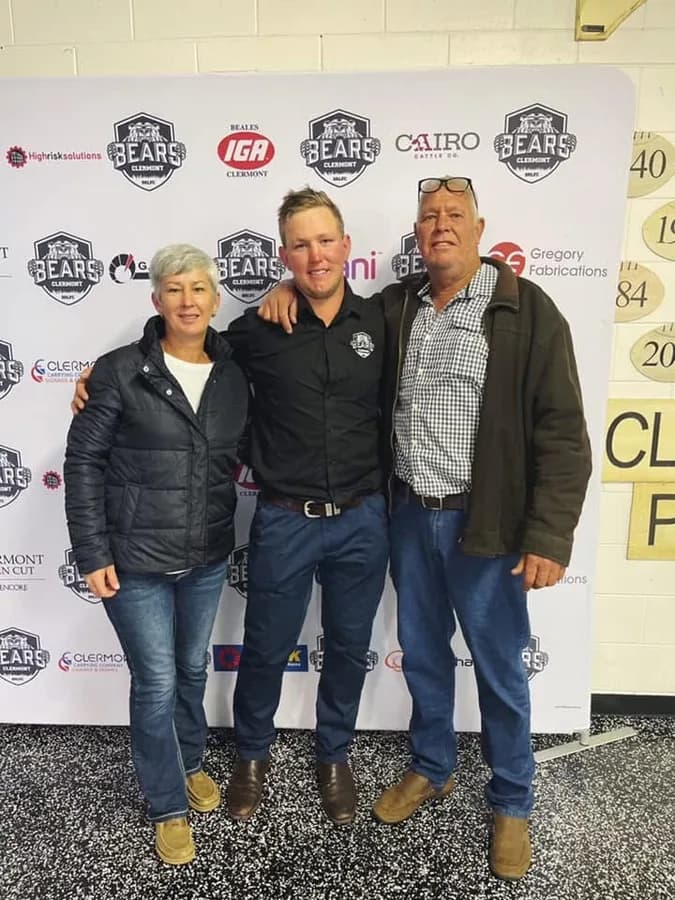Rugby league player Trent White with his parents, posing in front of a Clermont Bears Old Boys fundraising banner